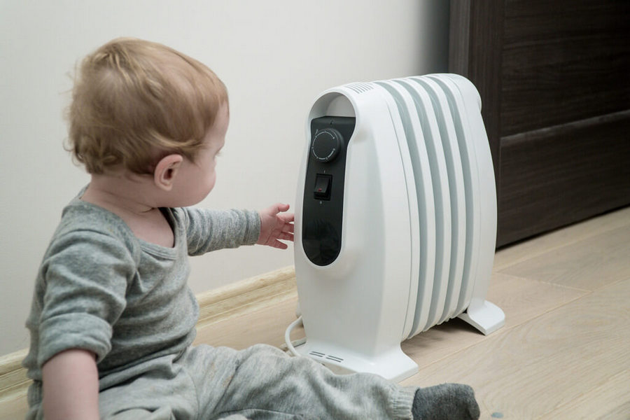 Little boy sitting near oil-filled radiator